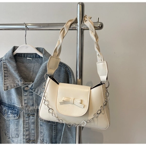 Detail of cream white shoulder bag featuring a decorative bow and floral metal chain