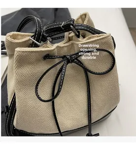 Detail of beige herringbone woven bucket bag with black leather base and drawstring closure