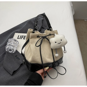 Detail of beige canvas bucket bag with black leather trim and plush cloud charm