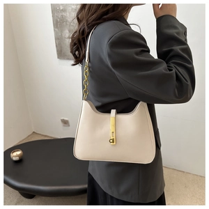 Détail du sac bandoulière crème avec chaîne dorée et fermoir métallique porté par un modèle