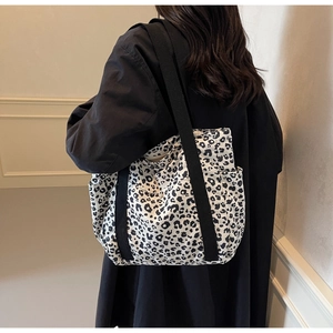 Detail of leopard print tote bag with black fabric straps shown on a model's shoulder
