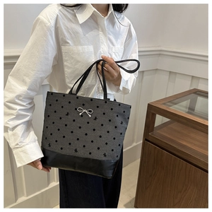 Detail of grey canvas tote bag with polka dots, bow embroidery, and black leather handles