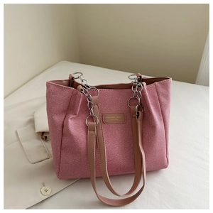 Detailed shot of pink woven tote bag with silver chain and leather strap on white fabric