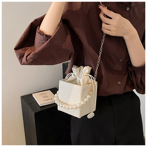 Detail of cream white bucket bag with pearl handle, chain strap and drawstring lining