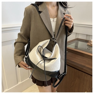 Detail of canvas bucket bag with black leather base, bow decor, and contrast stitching