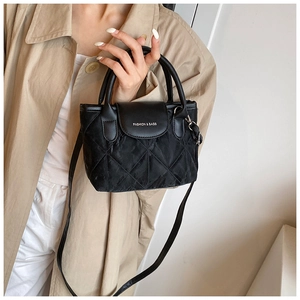 Detail of black quilted bucket bag with chain strap worn with a beige trench coat