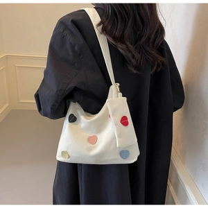 Detail view of white canvas tote bag with colorful heart patches and matching mini pouch
