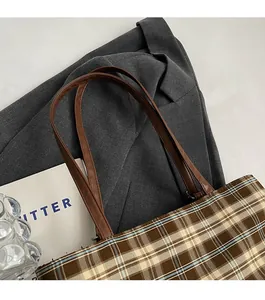 Detail of durable brown leather shoulder strap with sturdy metal ring on plaid tote bag