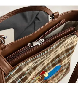 Close-up of smooth silver metal zipper and brown leather trim on plaid tote bag