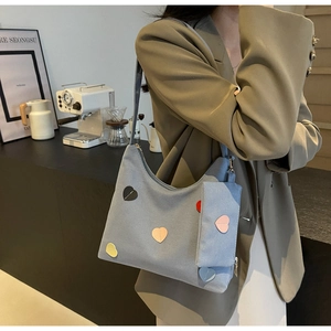 Blue canvas hobo tote bag with colorful heart patches and mini pouch set shown on model