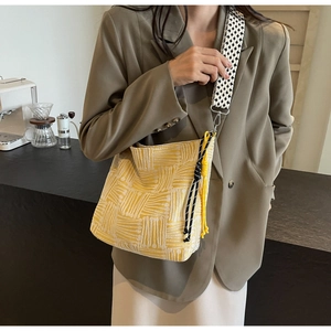 Detail of yellow canvas bucket bag with woven shoulder strap and decorative knot charm