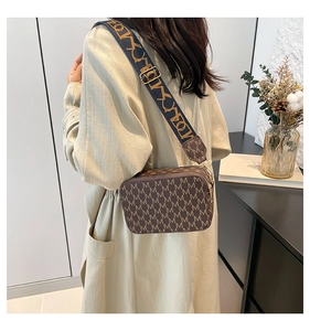 Macro detail of brown square crossbody bag featuring monogram print and wide woven strap