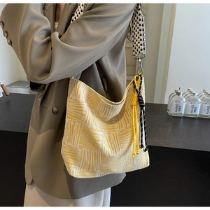 Close-up of striped canvas tote bag featuring checkerboard strap and woven rope charm