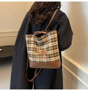 Detail of checkered canvas tote bag featuring dog embroidery and leather base on black coat