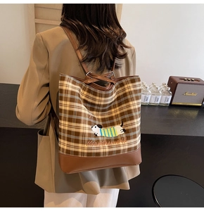 Detailed view of brown plaid bag with dog embroidery worn by model in casual suit