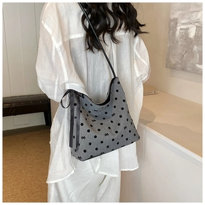 Close-up of a grey polka dot bucket bag with ribbon bow charm worn by a model