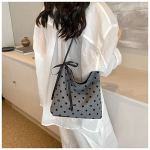 Polka dot hobo bag with large black ribbon bow on a model in a minimalist setting