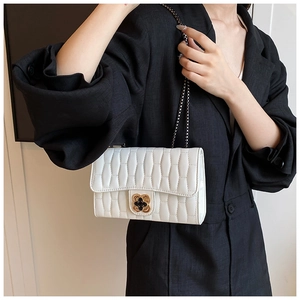 Detail of white pleated shoulder bag featuring a gold floral clasp and chain strap