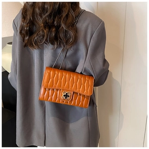 Close-up of orange quilted crossbody bag with clover twist lock and gold chain strap