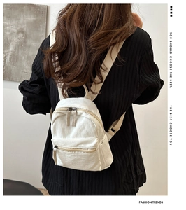 Detail view of mini nylon backpack showing textured straps and double zippers in beige
