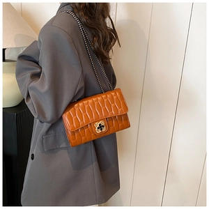 Close-up of quilted brown leather bag featuring a gold clover lock and chain strap