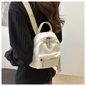 Detail view of a mini beige canvas backpack with zippered front pocket and straps