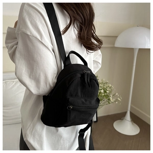 Mini sac à dos minimaliste en nylon noir porté par un mannequin dans une pièce chaleureuse