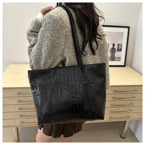 Detail of glossy crocodile pattern tote bag shown over the shoulder on a model