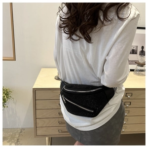Detail of black rhinestone chest bag with striped strap worn by model in casual setting