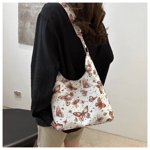Detailed view of white tote bag with red butterfly print worn on a female shoulder