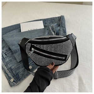 Detail of black rhinestone fanny pack with geometric wide strap on denim and book