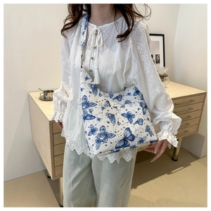 Close-up of white tote bag with blue butterfly print worn by a model in lace shirt