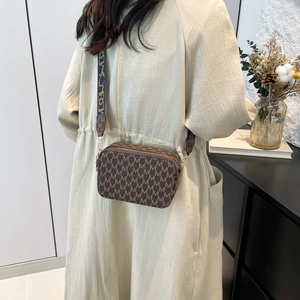 Brown camera crossbody bag with letter print and wide strap shown on a model