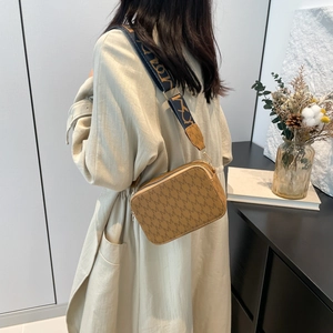 Brown camera crossbody bag with letter print and wide jacquard strap on a model