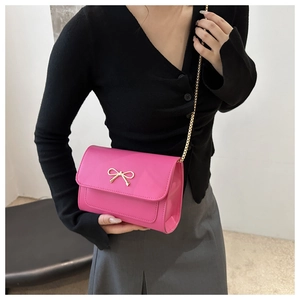 Detail of pink crossbody bag featuring a golden bow clasp and metallic chain strap