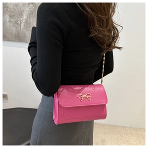 Detail of pink leather crossbody bag featuring a golden bow clasp and chain strap