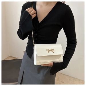 Close-up of a white luxury chain bag with golden bow buckle on a fashion model