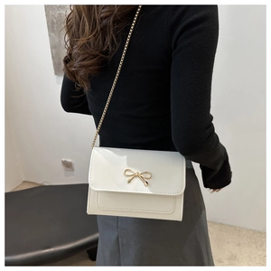 Detailed shot of white patent leather crossbody bag with golden bow and chain strap