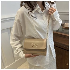Sac bandoulière kaki avec nœud doré porté sur chemise blanche pour référence de taille