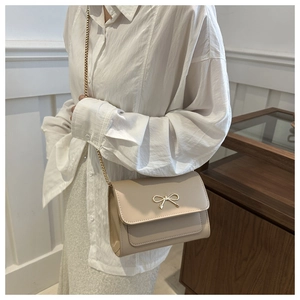 Detail showing elegant apricot square bag with gold bow clasp on white shirt outfit
