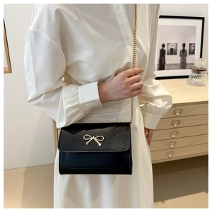 Detail of black mini crossbody bag with golden bow clasp and elegant chain strap