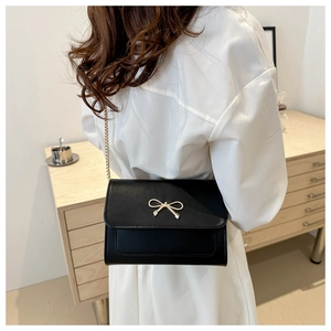 Elegant black leather crossbody bag with golden bow clasp and chain strap on a model