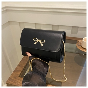 Detail of black crossbody bag with gold bow buckle and elegant metal chain strap