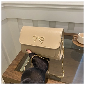 Detail of beige small square bag with gold bow clasp and metal chain on wooden desk