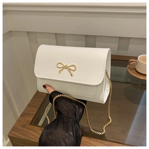 Detail of elegant white square handbag with golden bow accent and delicate chain strap