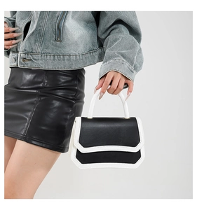 Detail of a black and white crossbody bag featuring gold hardware and a top handle