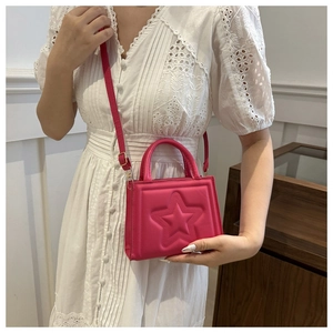 Model wearing a rose red crossbody bag with embossed star pattern and top handle