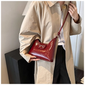 Nahaufnahme der burgunderroten Hobo-Tasche mit silberner Schleife auf beigem Mantel