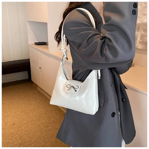 Detail of white glossy leather shoulder bag with silver bow ornament and knot strap detail