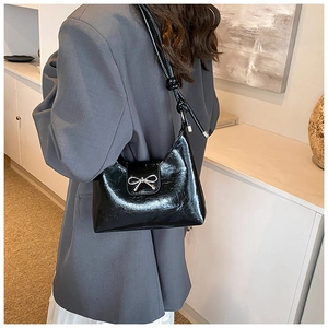 Glänzende schwarze Schultertasche mit silberner Schleife zu grauem Blazer-Outfit